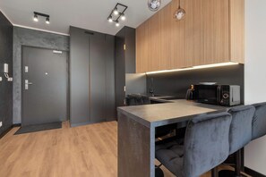 A modern kitchen with a dark countertop, wooden cabinets, and a microwave. - Modern Apartments with Balconies | Downtown (Gdańsk)