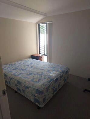 A bedroom with a bed, a small wooden cabinet, and a window with a metal grill.
