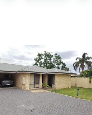 A single-story building with a garage, a paved driveway, and a fenced backyard.