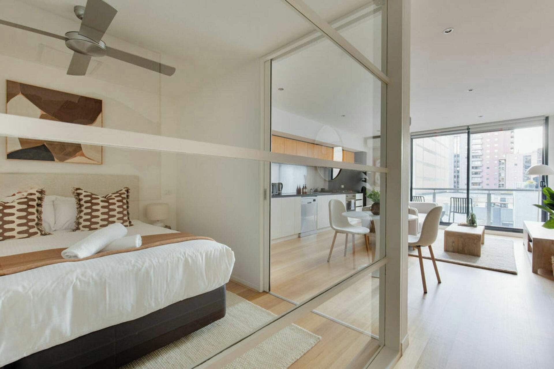 Une chambre d’hôtel moderne équipée d’un lit, d’un ventilateur de plafond, d’un coin cuisine et d’un balcon avec des sièges.