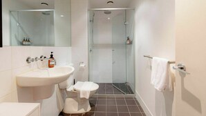 Een moderne badkamer met een douchecabine van glas, een witte wastafel en een toilet.