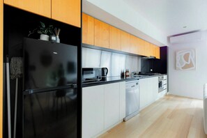 Een moderne keuken met een zwarte koelkast, witte kasten, een magnetron en een fornuis.