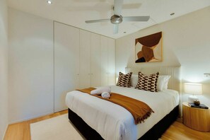 Een slaapkamer met een bed, een plafondventilator, een nachtkastje met een lamp en een kunstwerk aan de muur.
