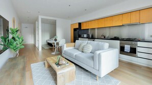 Een moderne woonkamer met een witte bank, een houten salontafel, en een eethoek met een witte tafel en stoelen.