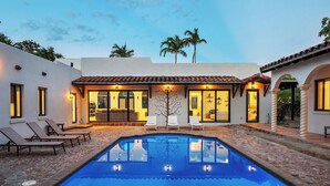 Ein Pool mit Liegestühlen, eine Terrasse und ein Gebäude mit großen Fenstern und Türen.