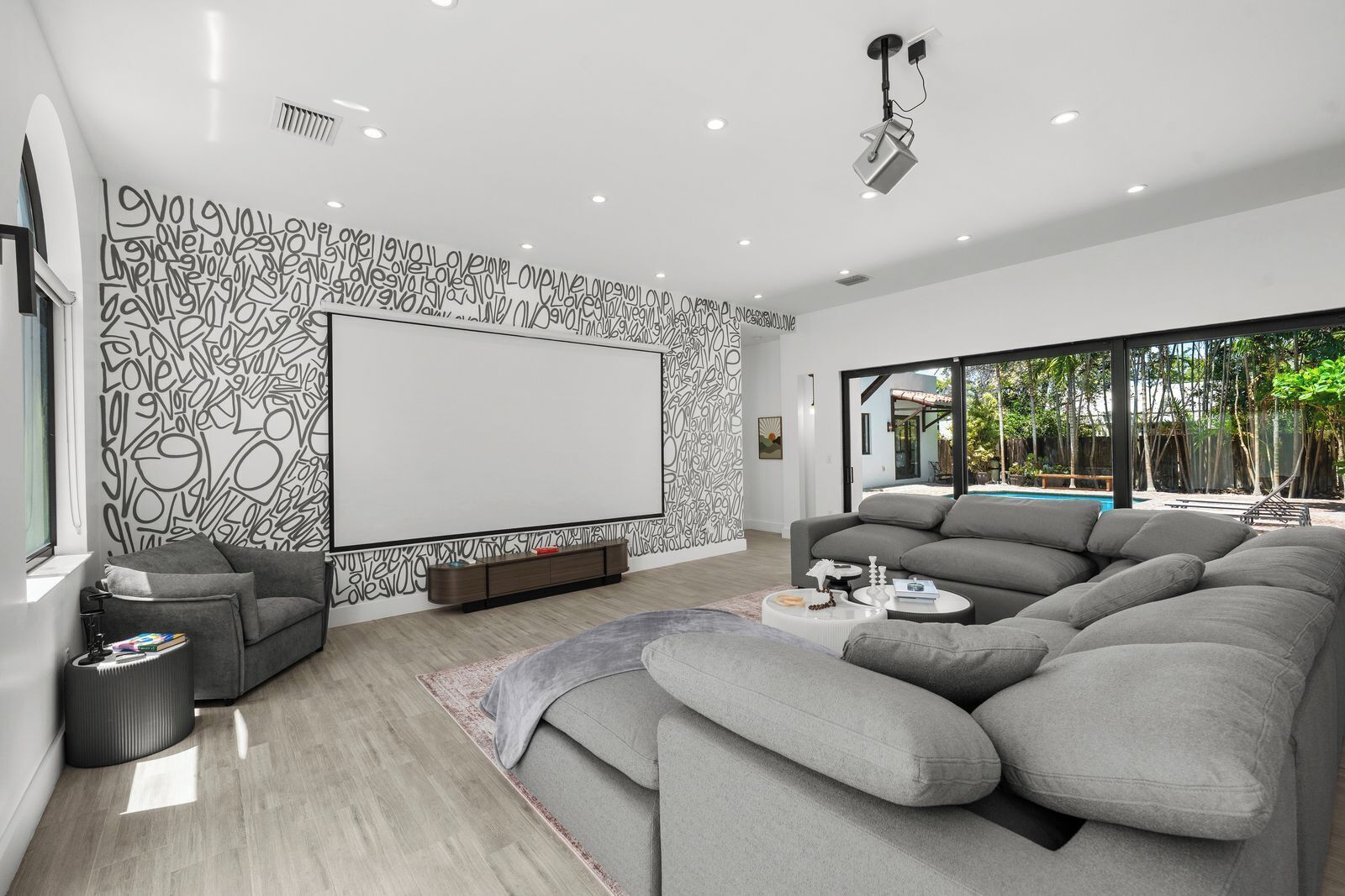 A modern living room with a sectional sofa, a flat-screen TV, and a large window overlooking a pool.