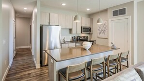 A modern kitchen with a central island, stainless steel appliances, and wooden chairs. - Landing Furnished Apartments Ocean Springs - Gulf Hills (Ocean Springs)