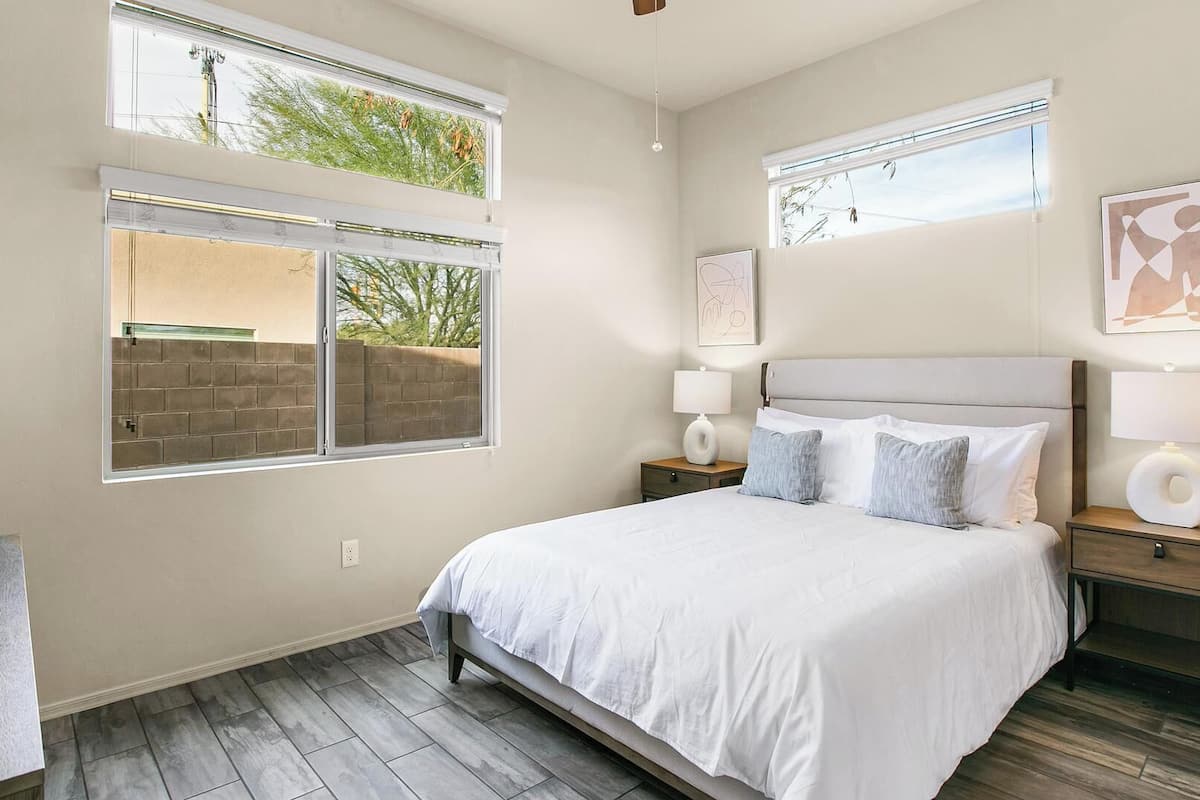 Une chambre à coucher comprenant un lit, deux tables de chevet, une commode, une fenêtre et une œuvre d’art accrochée au mur.