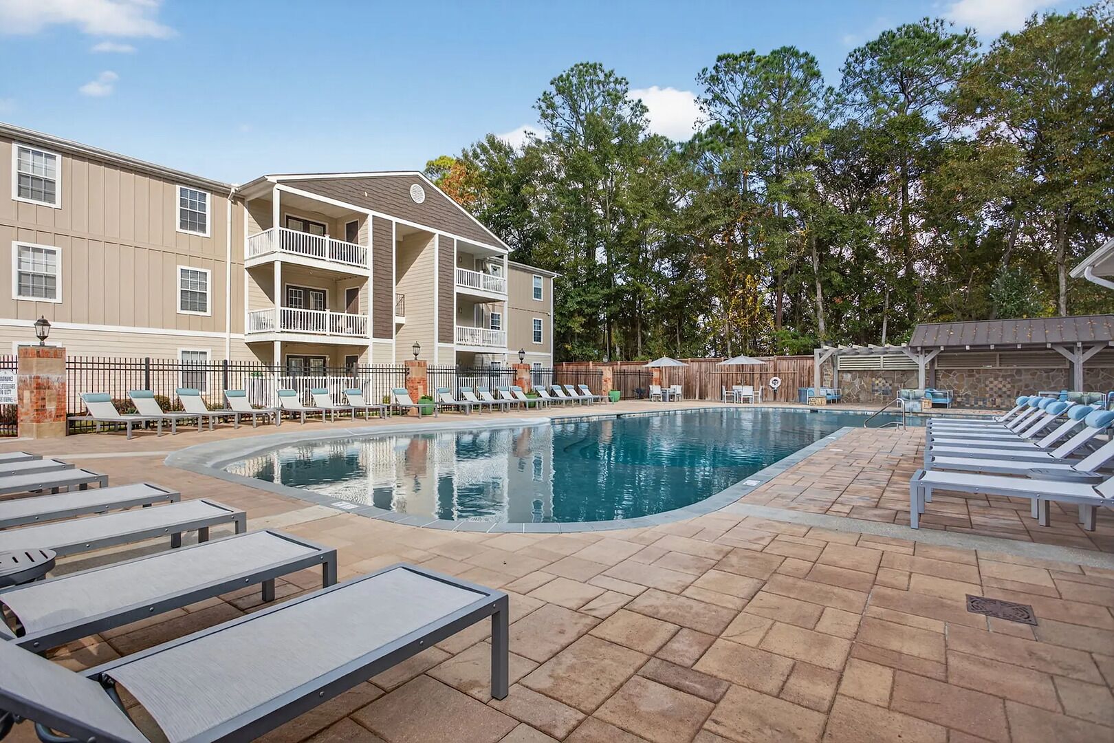 A pool area with lounge chairs, a swimming pool, and a building with balconies.