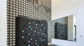 A climbing wall with a black surface and blue holds, labeled 'FREEDOM CLIMBER,' in a room with patterned walls. - Landing Beautiful 1bd, Yoga Studio (San Antonio)
