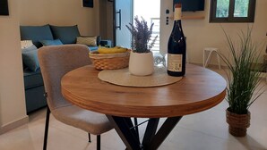 Een eetgedeelte met een ronde houten tafel, een rieten mand, een potplant en een fles wijn.