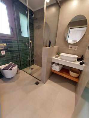 Un baño moderno con ducha envuelta en vidrio, un lavabo blanco y un espejo redondo.