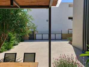 A covered outdoor area with a concrete floor, a wooden table, chairs, and a potted plant. - Elea Suites - Olive - Adelianos Kampos (Adelianos Kampos)
