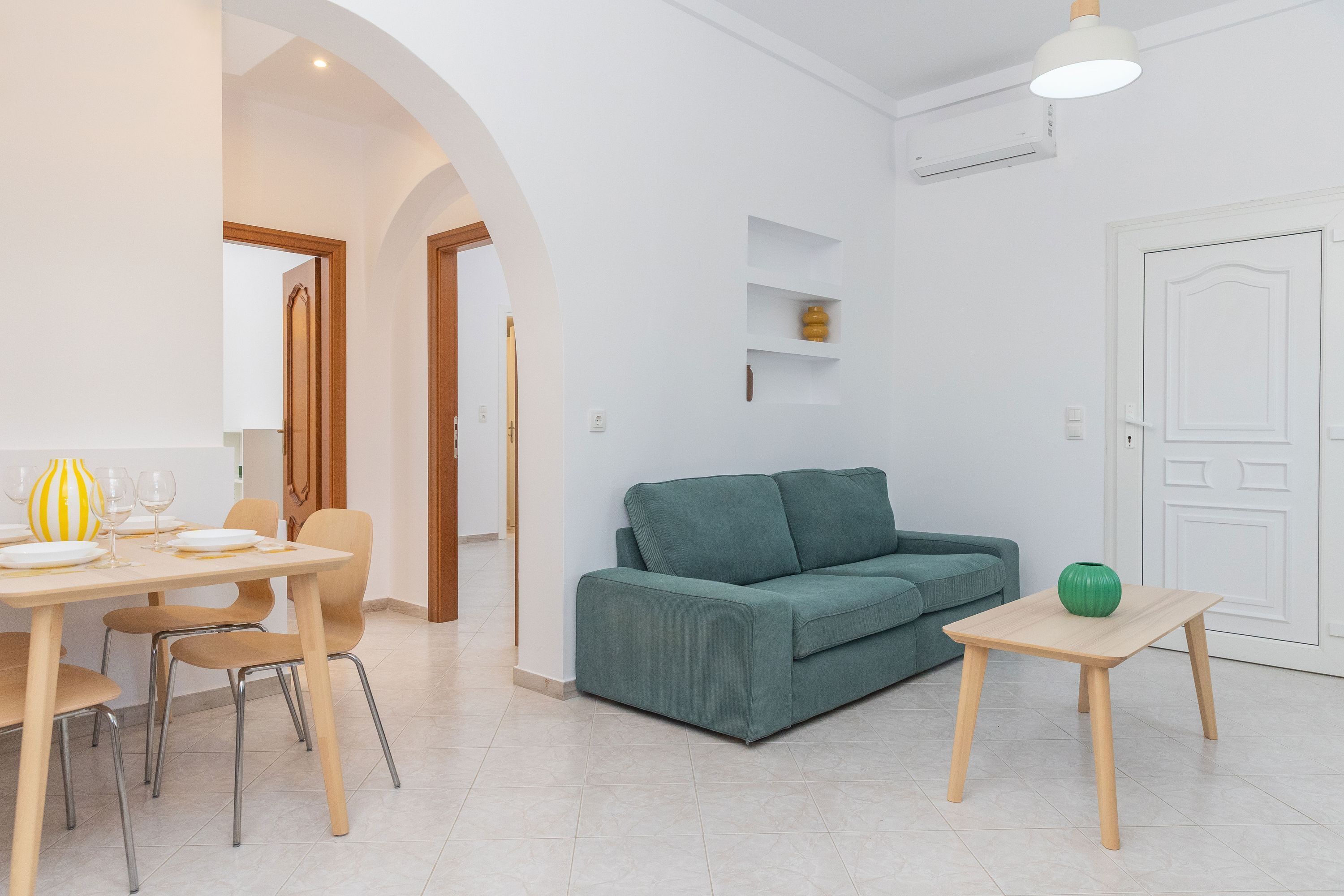 A modern living room with a green sofa, a wooden dining table with chairs, and a small side table with a green vase.