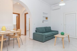 A modern living room with a green sofa, a wooden dining table with chairs, and a small side table with a green vase. - Grafeio - Two-Bedroom Deluxe Apartment wt Balcony (Naxos)