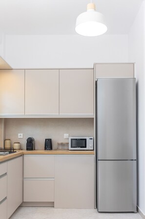 A modern kitchen with a stainless steel refrigerator, a microwave, and a coffee maker on the countertop. - Grafeio - Two-Bedroom Deluxe Apartment wt Balcony (Naxos)
