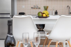 Eine moderne Küche mit Essbereich, ausgestattet mit einem weißen Tisch, Stühlen und einer Obstschale auf der Arbeitsplatte.