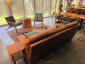 A spacious living area with a leather sofa, wooden chairs, a dining table, and a large window offering a view of the outdoors. - Spacious private modern 4-bedroom house in beautiful natural setting in Brooklin (Brooklin)