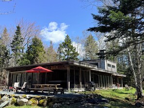 A cabin with a covered patio, a stone wall, and a view of the surrounding forest. - Spacious private modern 4-bedroom house in beautiful natural setting in Brooklin (Brooklin)