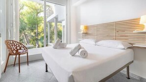 A hotel room with a bed, a chair, a window with a view of trees, and a wooden headboard. - Hostdomus - Queen Suite (Marina di Andora)