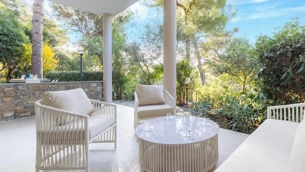 A covered outdoor seating area with wicker furniture and a round table, surrounded by greenery and trees. - Hostdomus - Queen Suite (Marina di Andora)