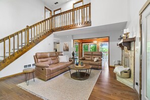 A spacious living room with a wooden staircase, leather sofas, a round coffee table, and a fireplace. - Mountain Views + Fire pit | 10 Min to BR/Yoga Room - Holiday Home (Blue Ridge)