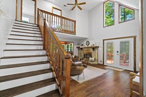 A spacious living area with a wooden staircase, a fireplace, and a view through large windows. - Mountain Views + Fire pit | 10 Min to BR/Yoga Room - Holiday Home (Blue Ridge)