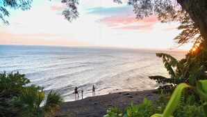 Uma praia com pessoas, vegetação e um pôr do sol.