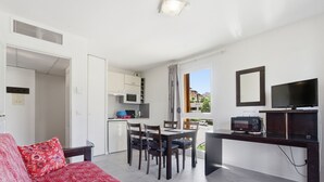 A compact living space with a kitchenette, a dining area, a TV, and a sofa with a patterned cover. - Flat with a swimming pool and a balcony with mountain views (Grasse)