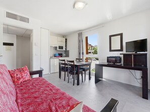 A compact living space with a kitchenette, a dining area, a TV, and a sofa with a patterned cover. - Flat with a swimming pool and a balcony with mountain views (Grasse)