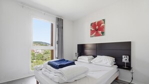 A bedroom with a bed, a window with curtains, a headboard, and a wall-mounted artwork. - Flat with a swimming pool and a balcony with mountain views (Grasse)