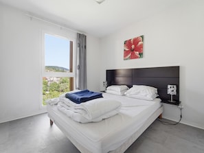 A bedroom with a bed, a window with curtains, a headboard, and a wall-mounted artwork. - Flat with a swimming pool and a balcony with mountain views (Grasse)