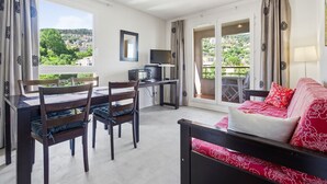 A room with a dining table, chairs, a TV, a sofa, and a balcony with a view. - Flat with a swimming pool and a balcony with mountain views (Grasse)