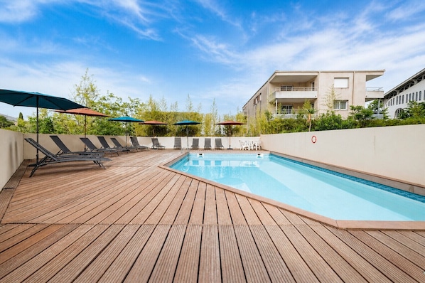 A rooftop pool with wooden decking, lounge chairs, and umbrellas. - Flat with a swimming pool and a balcony with mountain views (Grasse)