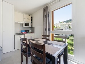A compact kitchen with modern appliances, a dining table with chairs, and a large window offering a view of buildings and greenery. - Flat with a swimming pool and a balcony with mountain views (Grasse)