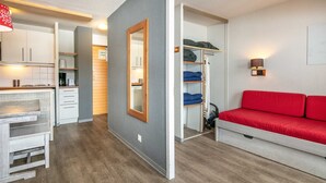Ein kompakter Wohnraum mit Küchenzeile, einem Spiegelkleiderschrank, einem roten Sofa und einem kleinen Tisch.