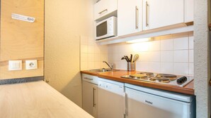 Een kleine keuken met witte kastjes, een magnetron, een fornuis en een vaatwasser.