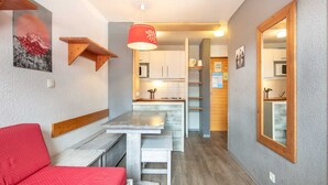 Een ruimtelijk ingerichte woonruimte met kitchenette, een eethoek en een rode bank.