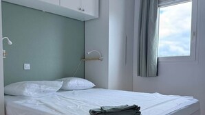 Ein Schlafzimmer mit Bett, Holz-Kopfteil, weißen Schränken, einem Fenster mit Vorhängen und einer Lampe.