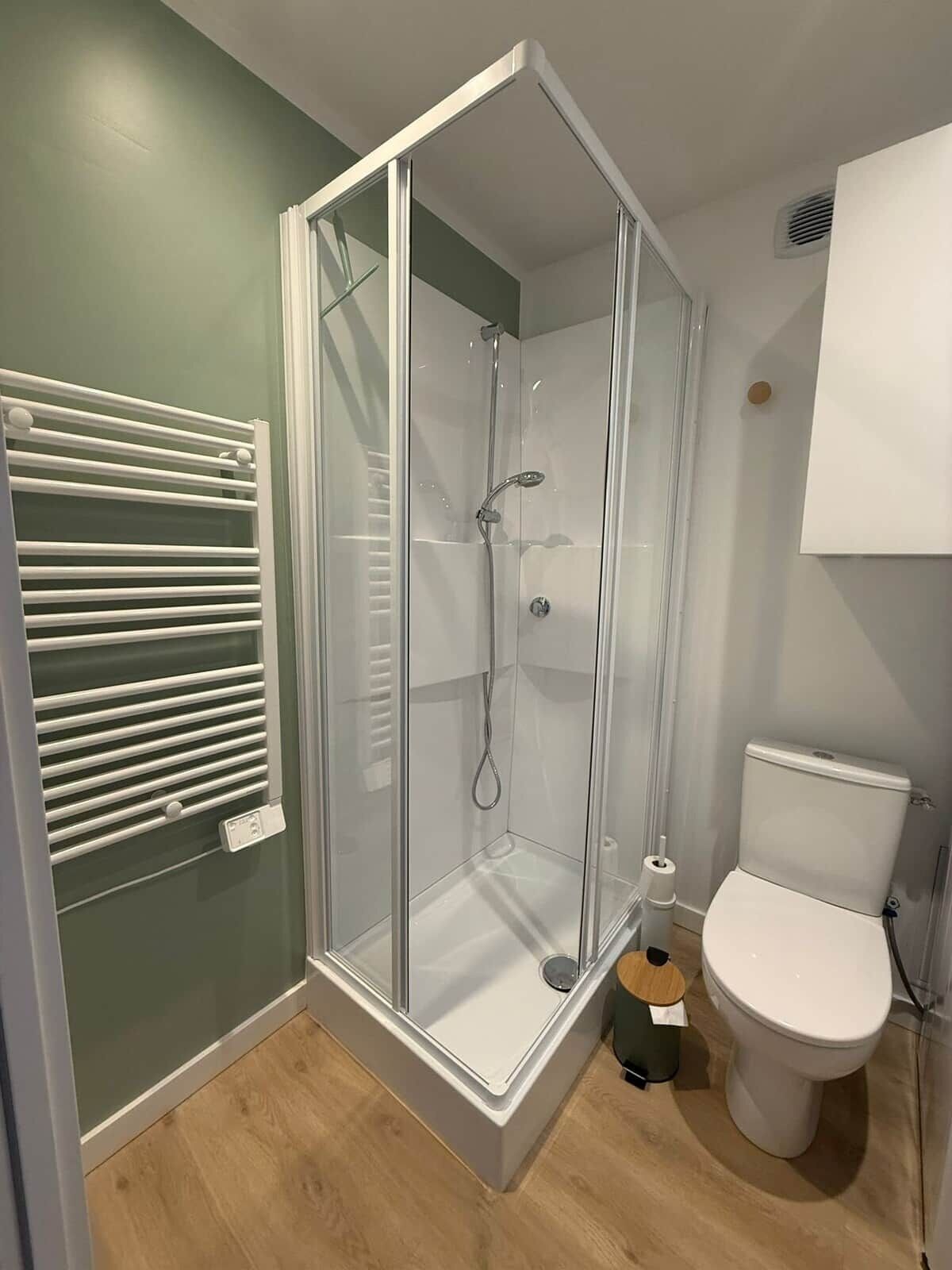 Une salle de bain moderne avec une douche à parois de verre, des toilettes blanches et un porte-serviettes.
