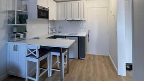 Eine kleine Küche mit weißen Schränken, einem Esstisch und einem Kühlschrank.