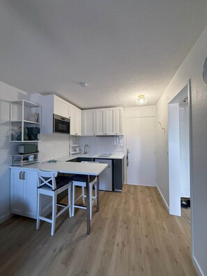 A compact kitchen with white cabinets, a small dining table, and a refrigerator. - Surf & Sun - Cozy One-Bedroom Apartment Near the Ocean (Soustons)