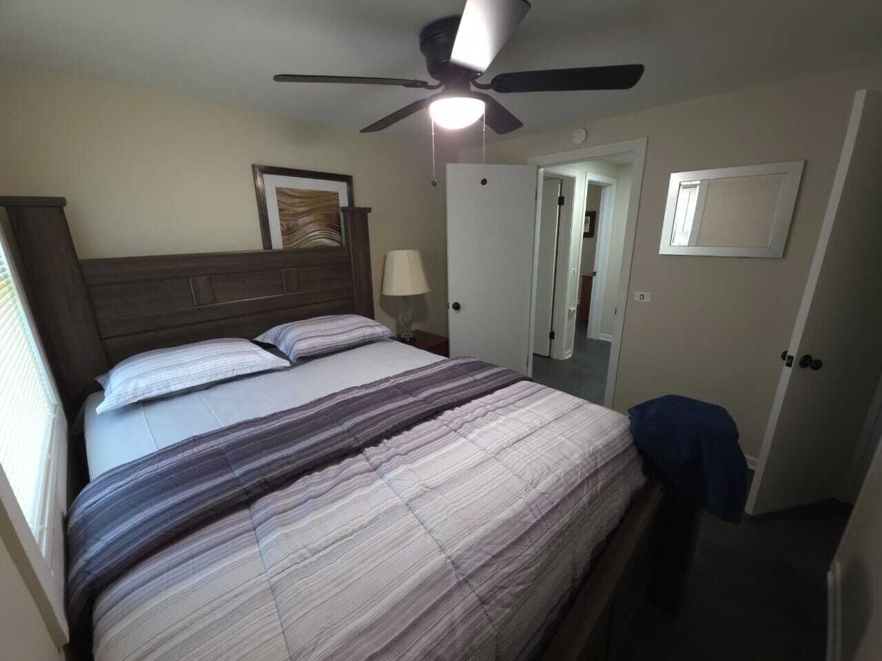 A bedroom with a bed, a ceiling fan, a nightstand, a lamp, and a door.