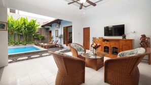 Una sala de estar moderna con piscina, muebles de mimbre, ventilador de techo y televisor de pantalla plana.