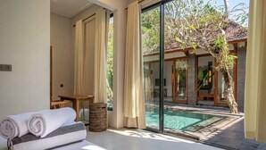 A modern room with a large sliding glass door leading to a pool area, a bed with rolled towels, and a small table. - Mimosa villa (Kerobokan)