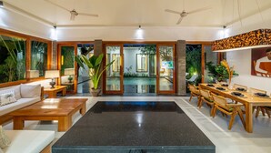 A spacious living area with a central black marble table, wooden furniture, and a view into a kitchen and dining area. - Mimosa villa (Kerobokan)