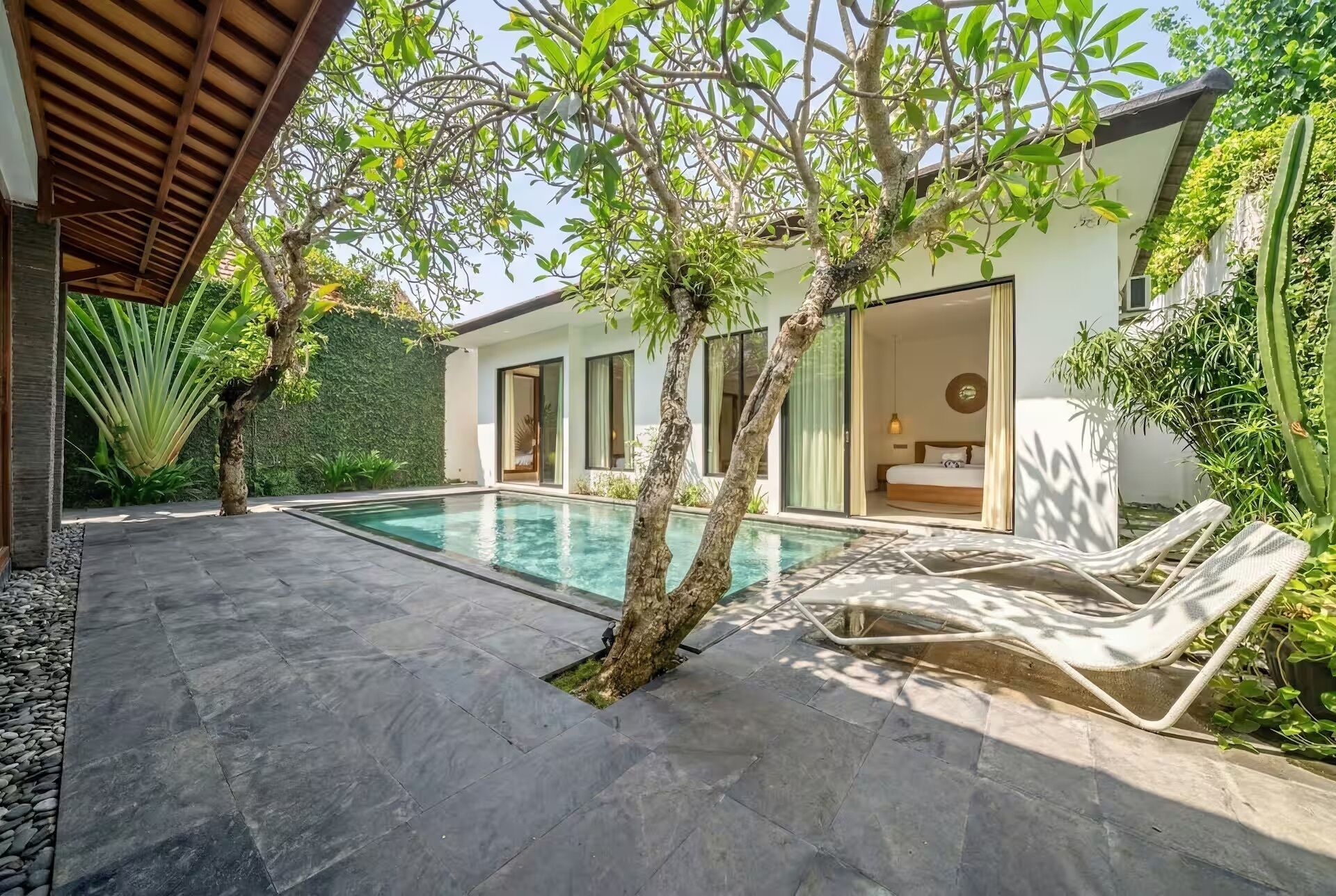 Een modern huis met een zwembad, een overdekt terras en een slaapkamer met een bed en nachtkastje.