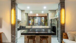 A modern kitchen with a central island, two bar stools, and a seating area with a sofa. - Mimosa villa (Kerobokan)