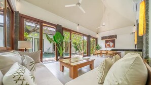 A modern living room with a sofa, coffee table, and a dining area with chairs and a table. - Mimosa villa (Kerobokan)