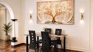 A dining area with a table and chairs, a large framed artwork of a tree, and wall-mounted lighting. - Room-tranquil Studio Retreat With Pool a (Westville)